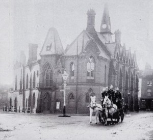 Firemen burst from the Town Hall to attend another fire, circa 1900.  They were relocated in 1969